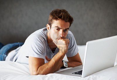 8233634-portrait-of-a-thoughtful-young-man-using-laptop-while-lying-on-bed-at-home-indoor-3831258